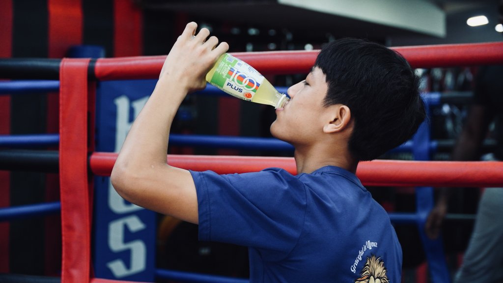 Young boxer drinking an isotonic drink to stay hydrated during training at King of Strength boxing gym.