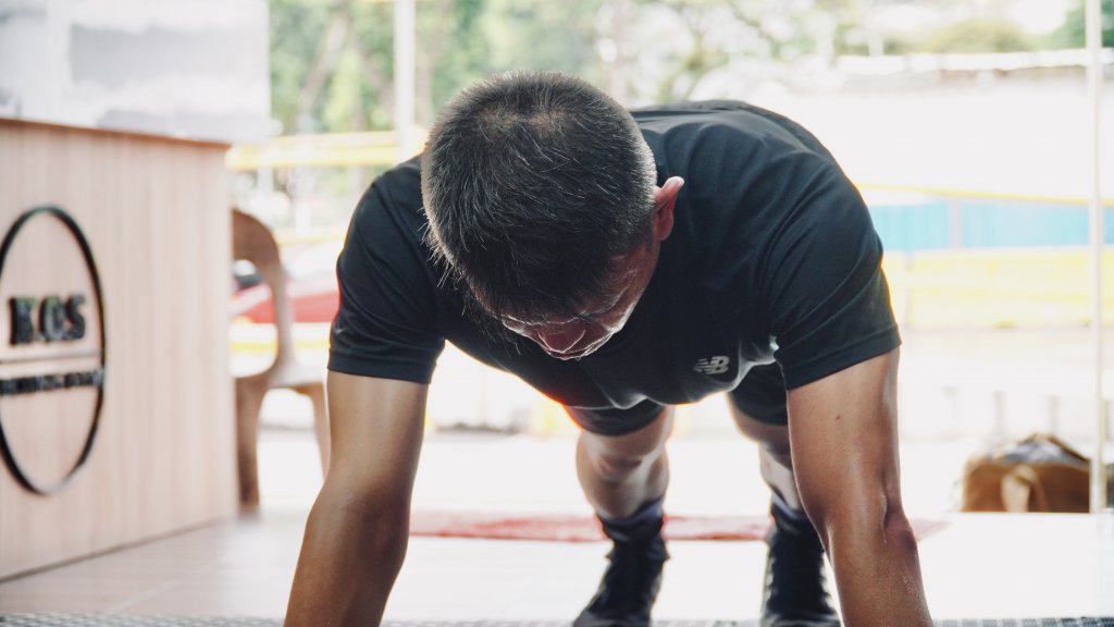 Man performing push-ups at boxing gym, with good posture and form emphasizing strength training and injury prevention.