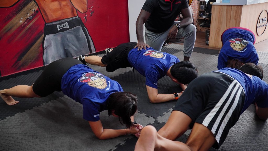 Group of people performing plank exercises under the supervision of a coach at King of Strength boxing gym.